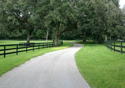 Paved path between two fenced off grassy fields at Country Road Farm in Ocala, Florida.